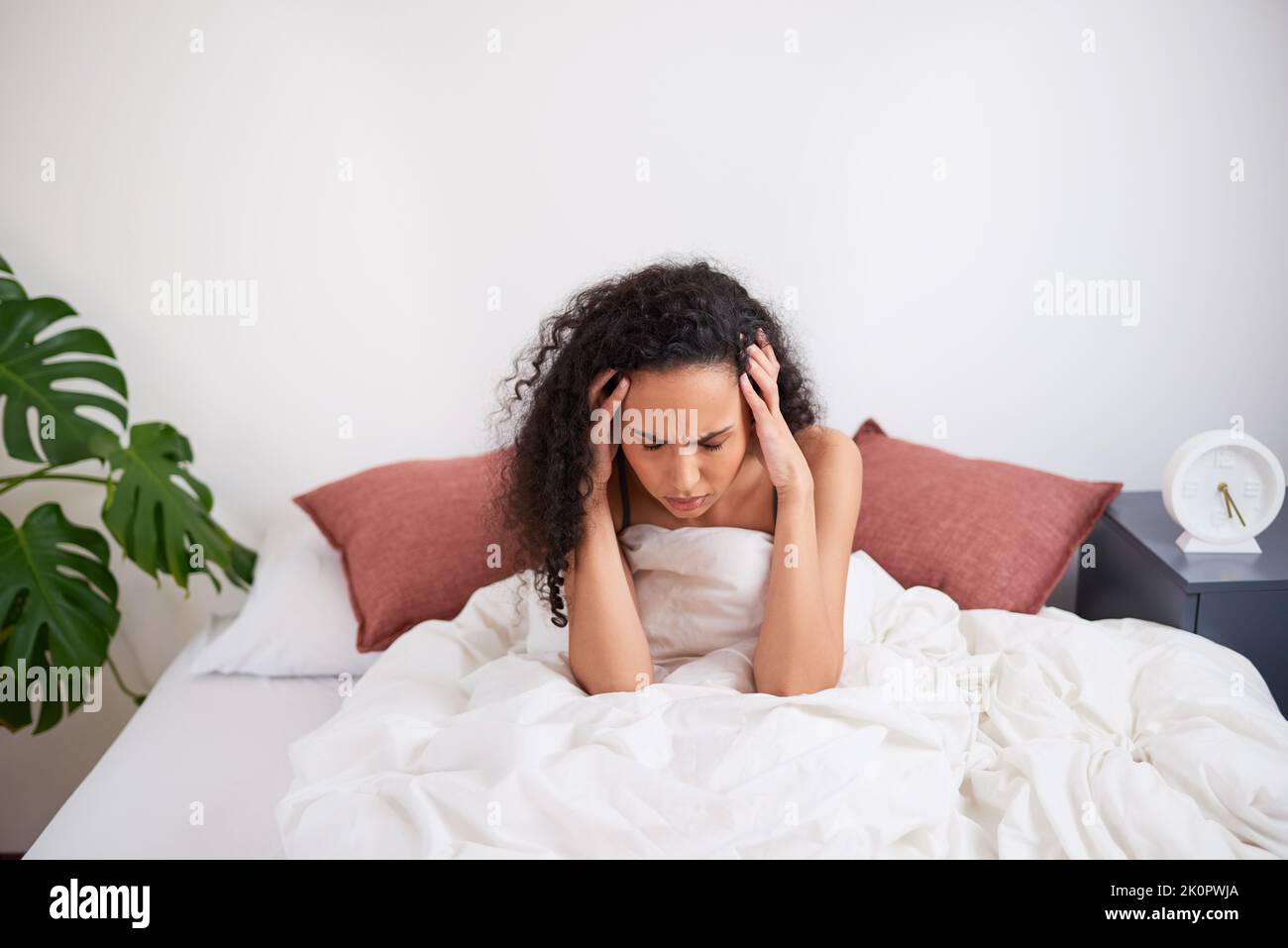 Una giovane donna multietnica si siede con la testa nelle mani che lottano per svegliarsi a letto Foto Stock