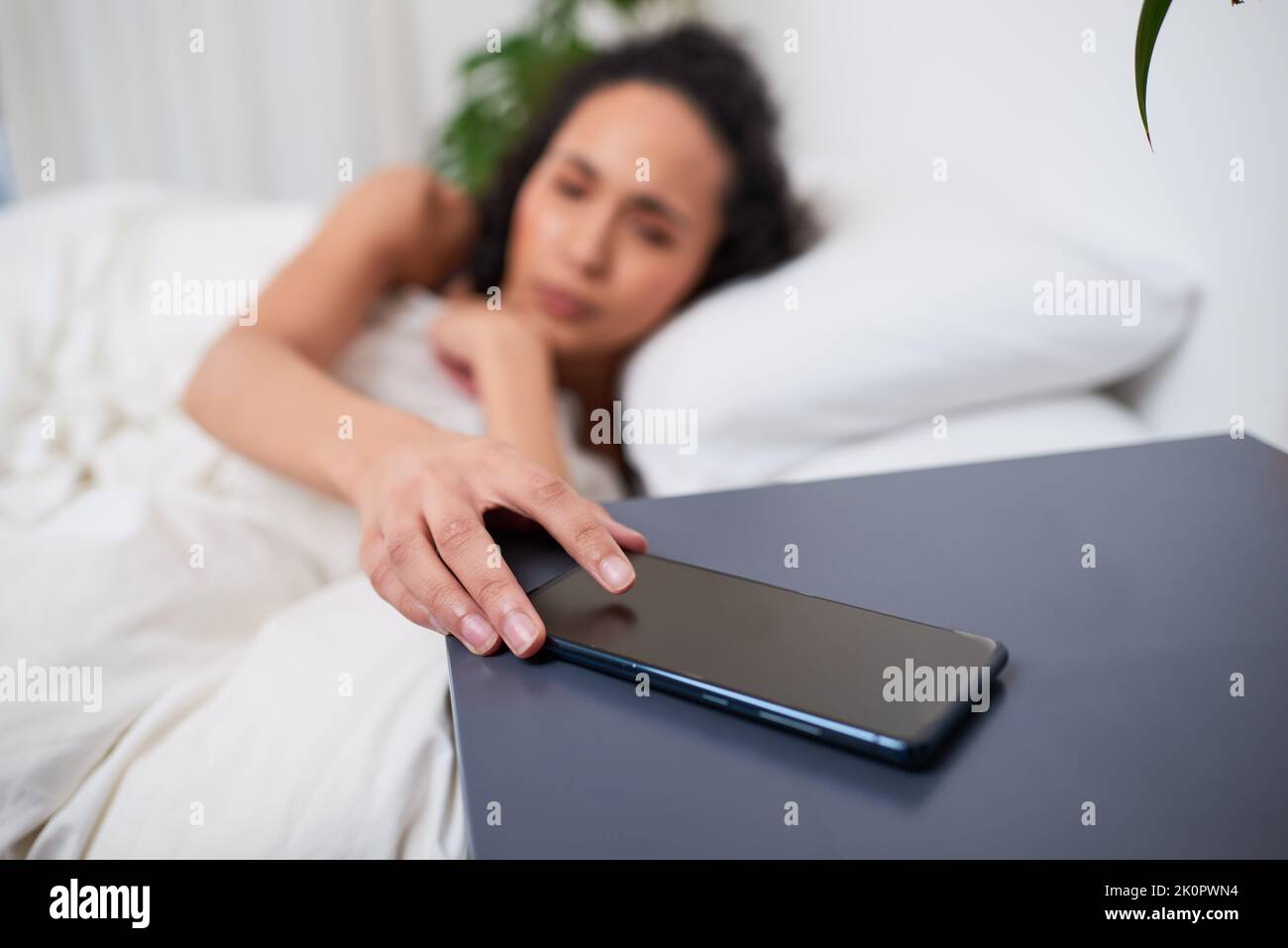 Fuoco selettivo sul cellulare come donna si sveglia a letto Foto Stock