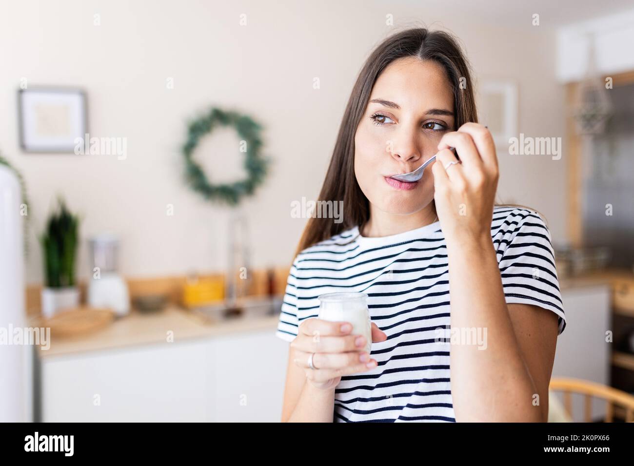 Giovane donna che mangia yogurt a casa Foto Stock