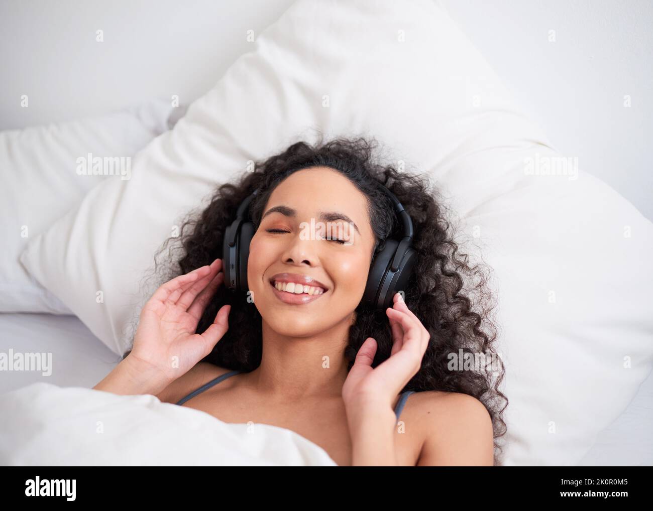 Un'immagine di una giovane donna multietnica sdraiata a letto con le cuffie Foto Stock