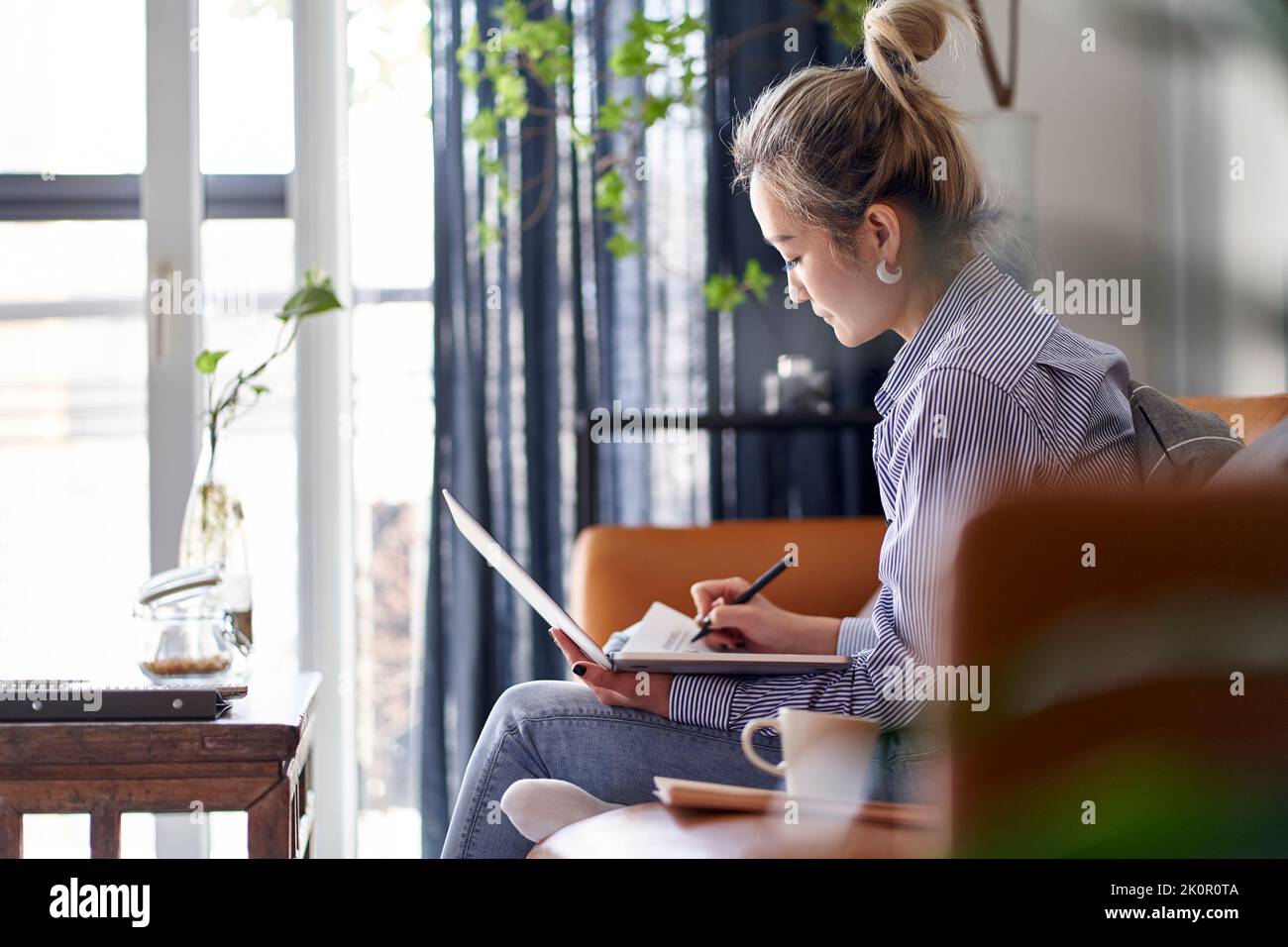 donna asiatica professionista matura che lavora su un documento cartaceo da casa utilizzando un computer portatile, vista laterale Foto Stock