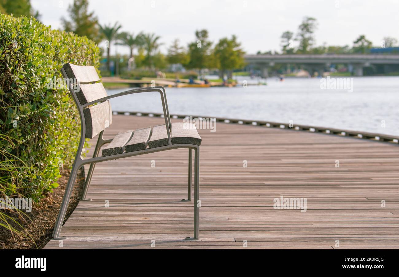 Concentratevi su una panca in metallo con stecche in legno su una passerella e uno sfondo sfocato di un ponte e acqua. Foto Stock