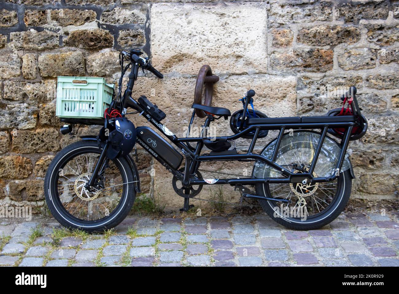 Una bici elettrica a tre posti, incatenata a una gigantesca catena su un muro di pietra. Ciottoli Foto Stock