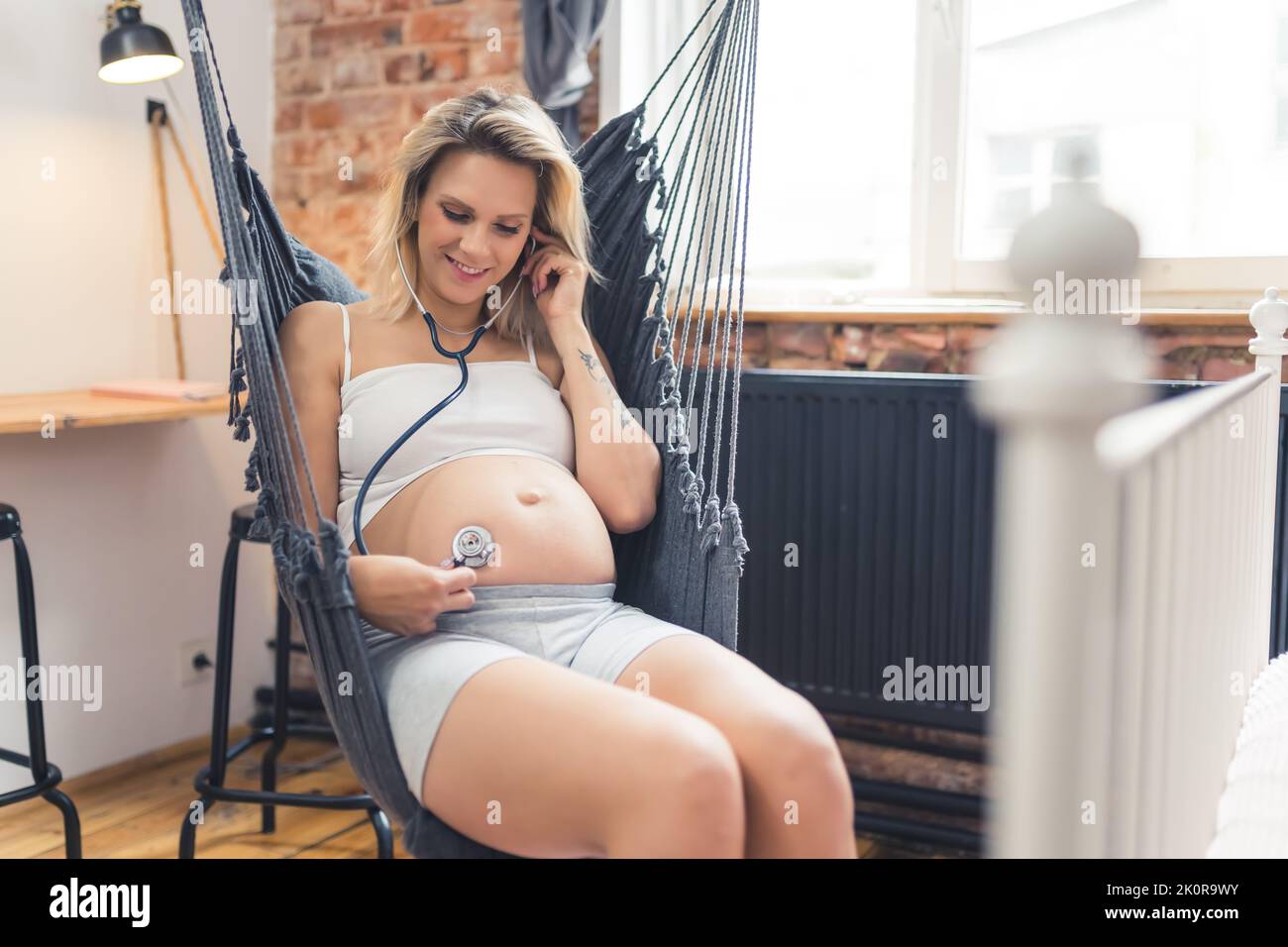 Giovane donna incinta sposata che ascolta il battito cardiaco del proprio bambino con uno stetoscopio a casa. Felice presto-essere madre. Foto di alta qualità Foto Stock