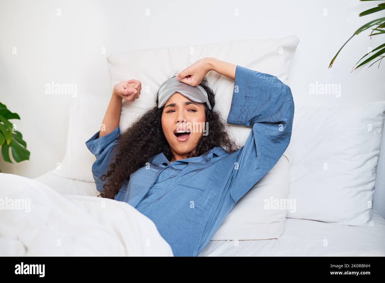 Una giovane donna multietnica si allunga e si sbadiglia con maschera del sonno Foto Stock