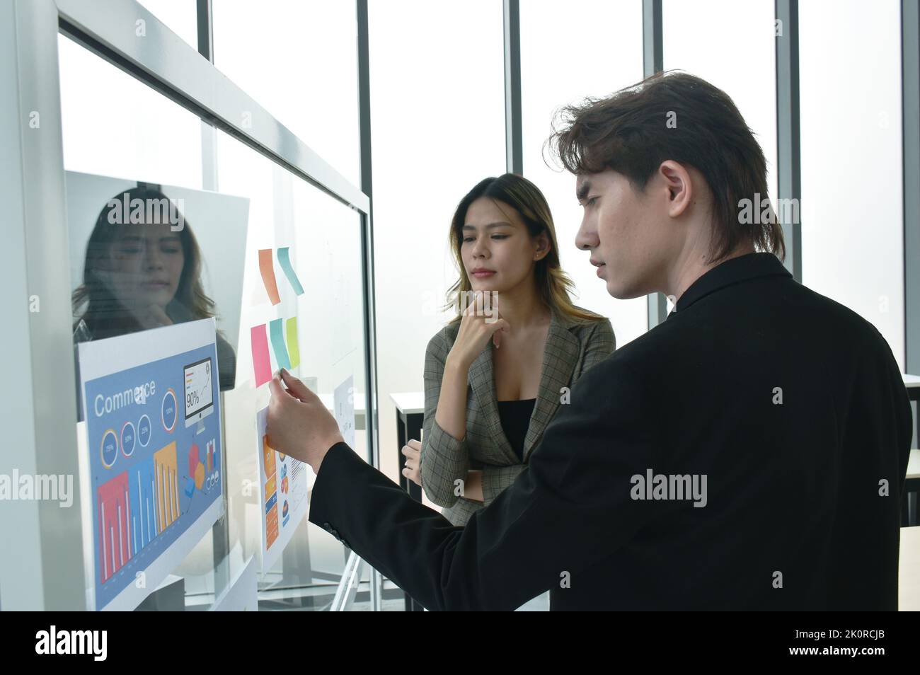 Uomo e donna asiatico di affari che guardano il bastone della nota della carta sul bordo di vetro per discutere e lavorare nell'ufficio Foto Stock