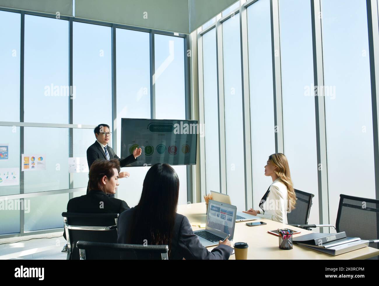 Uomo d'affari asiatico che presenta il lavoro sullo schermo della televisione con una donna che guarda il computer portatile nella sala riunioni dell'ufficio Foto Stock
