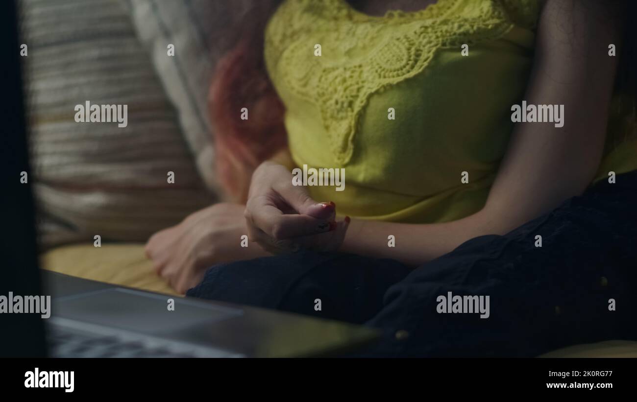 Primo piano ha girato le mani di una donna con disabilità fisica che gestiva durante la conversazione tramite videochiamata online sul notebook seduto sul divano Foto Stock