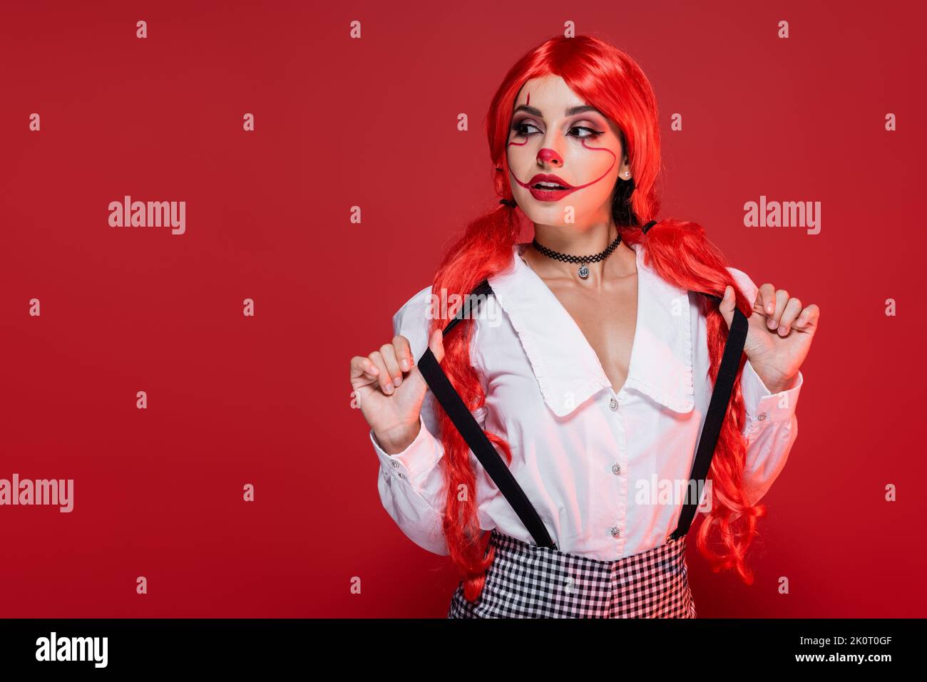 giovane donna rossa in halloween trucco che tocca sospensori e guardando modo isolato sul rosso Foto Stock