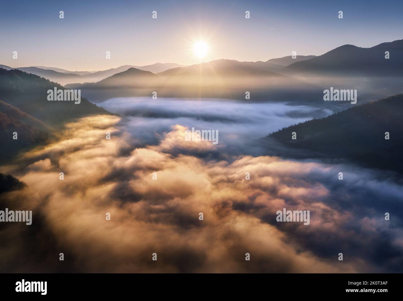 Montagne nelle nubi basse all'alba in estate. Vista aerea Foto Stock