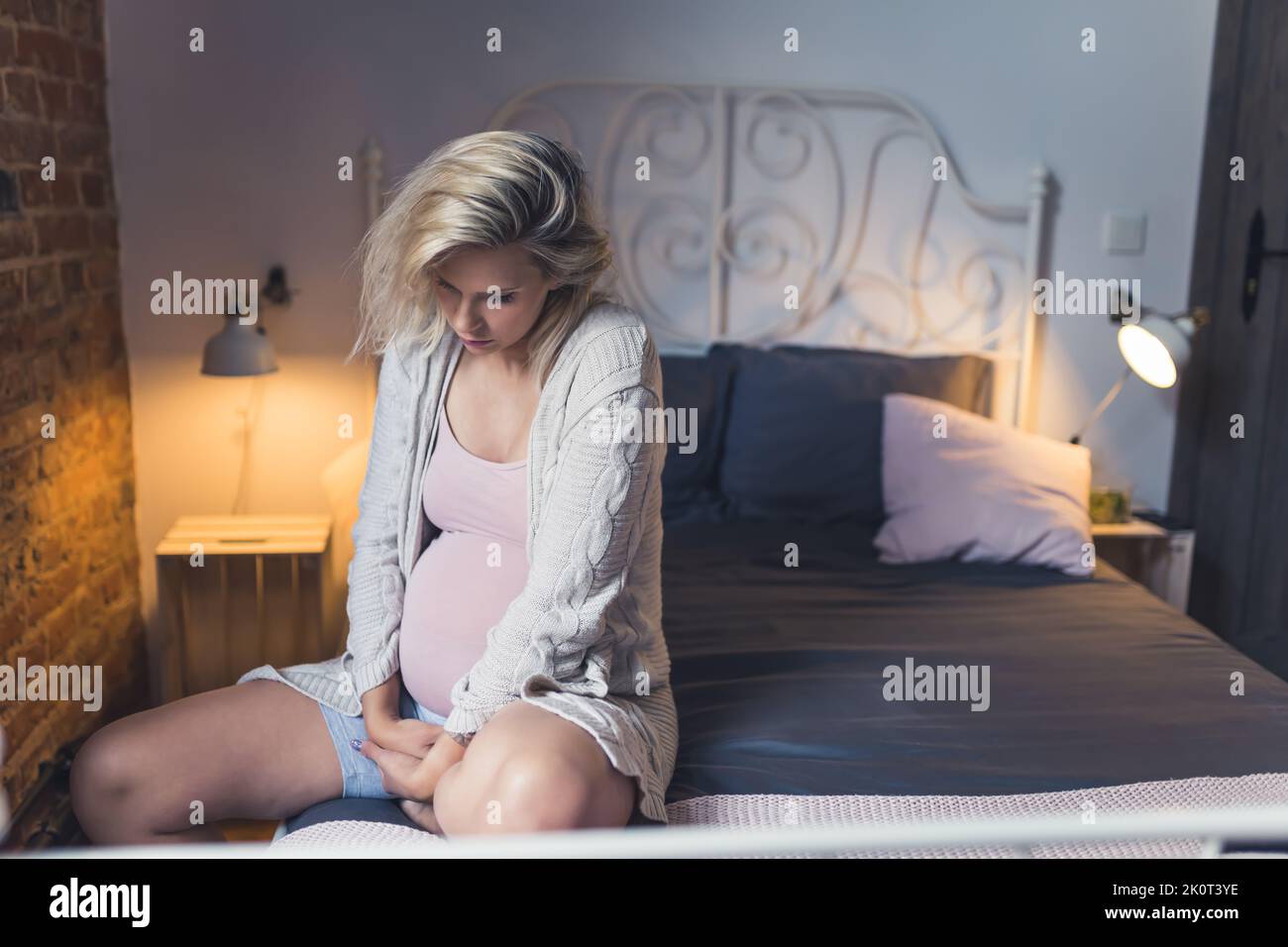 Donna in gravidanza matura che lotta con insonnia, stanchezza e affaticamento durante gli ultimi mesi di gravidanza. Donna seduta su un letto e che sostiene il ventre con le mani. Foto di alta qualità Foto Stock