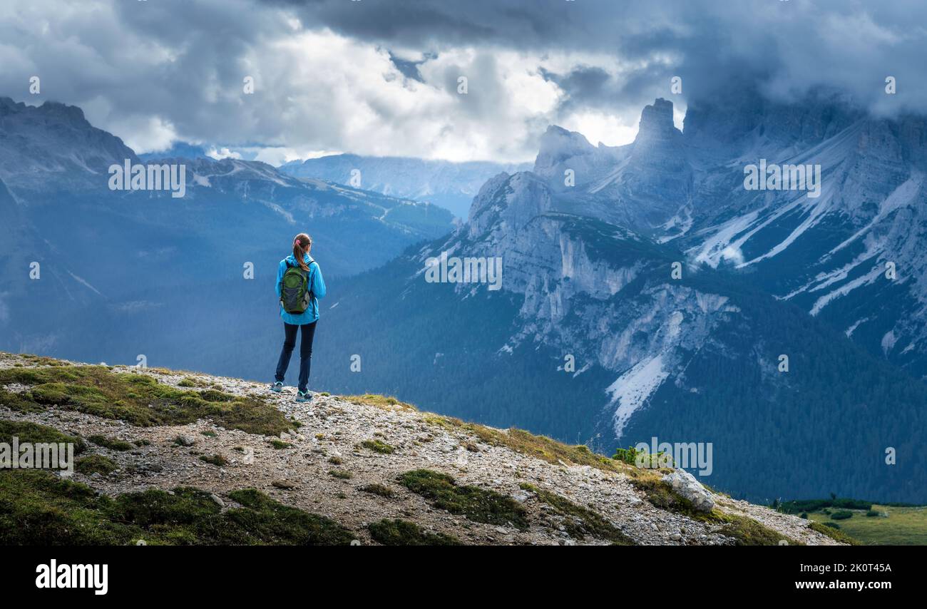 Ragazza con zaino sulla collina che guarda le montagne al tramonto Foto Stock
