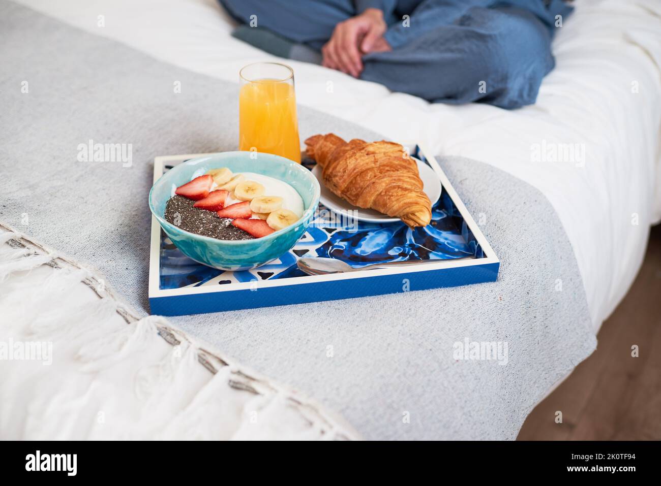 Primo piano del vassoio della colazione con croissant, frutta ciotola a letto con donna seduta Foto Stock