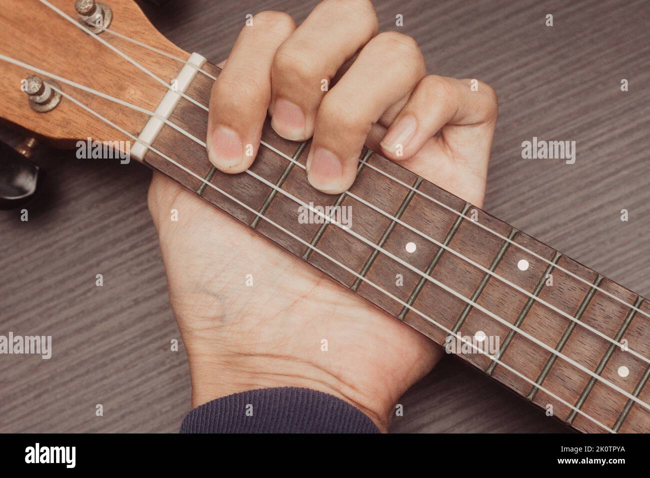 ukulele in primo piano con la mano di mettere accordi. L'accordo è G. strumento portatile a corda. Concetto di creazione musicale. Sfondo isolato in legno Foto Stock