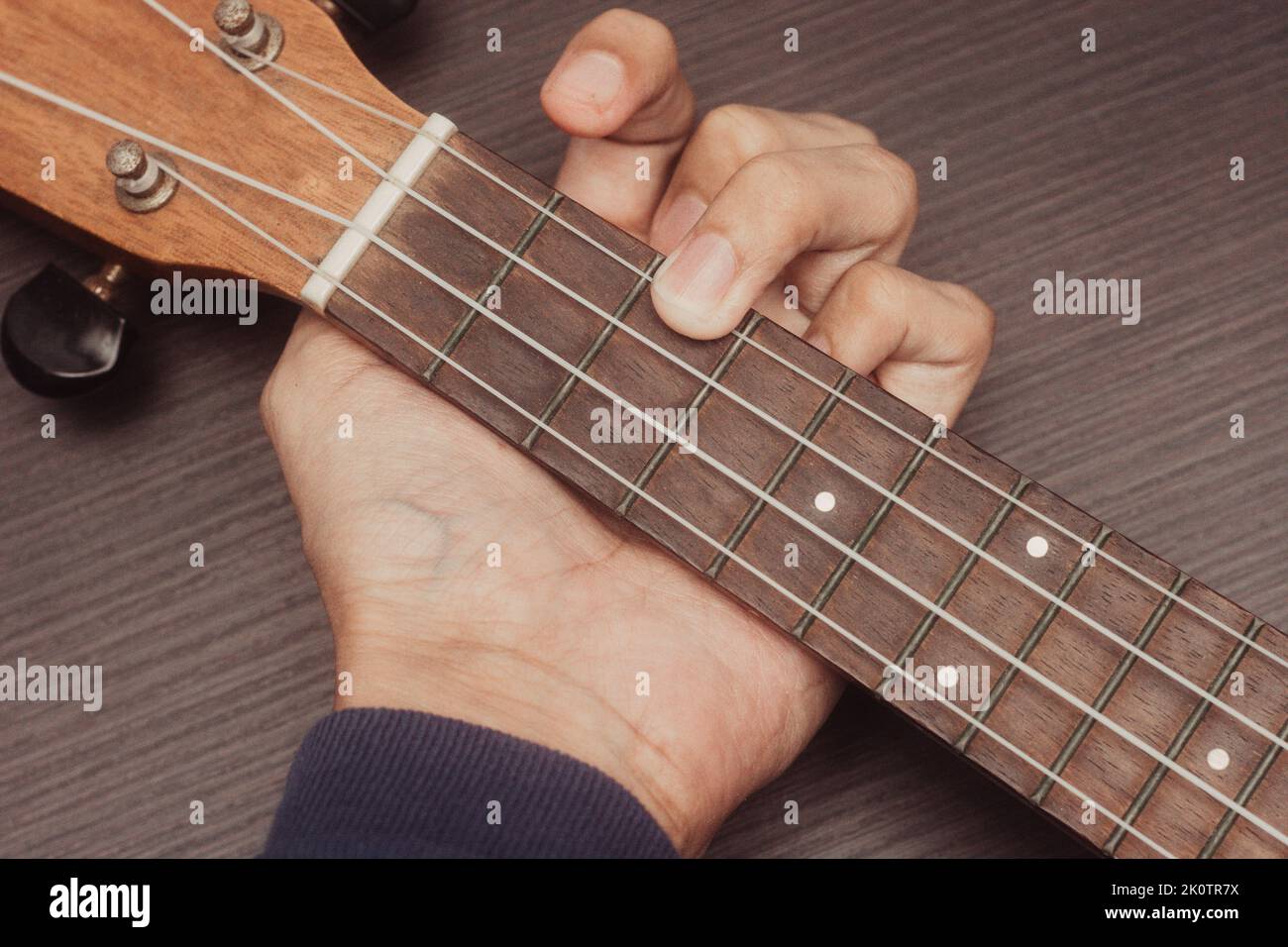 ukulele in primo piano con la mano di mettere accordi. L'accordo è C. strumento portatile a corda. Concetto di creazione musicale. Sfondo isolato in legno. Foto Stock