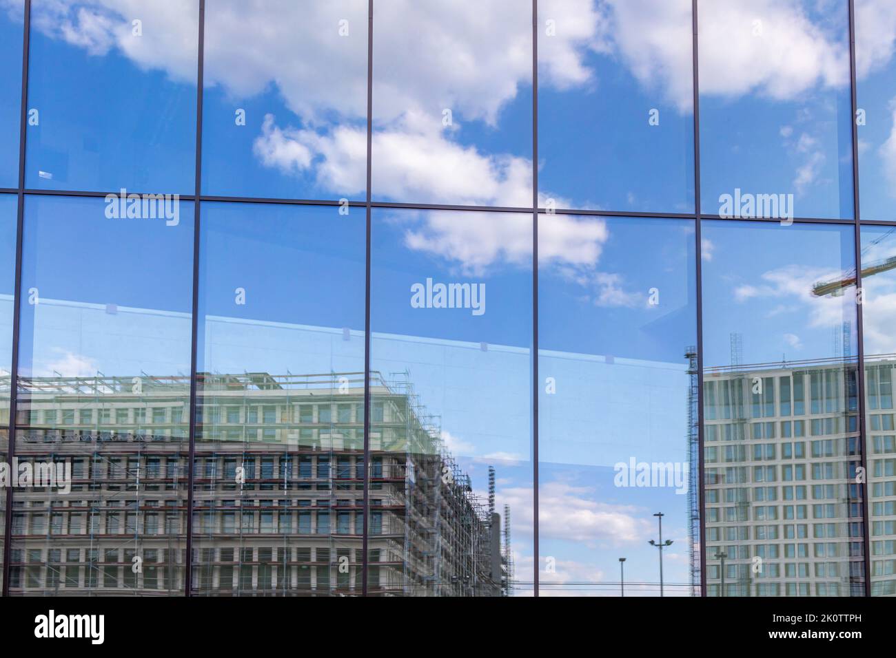 Riflesso di un grande cantiere con nuovi edifici e cielo leggermente nuvoloso in una facciata di vetro di un edificio moderno Foto Stock