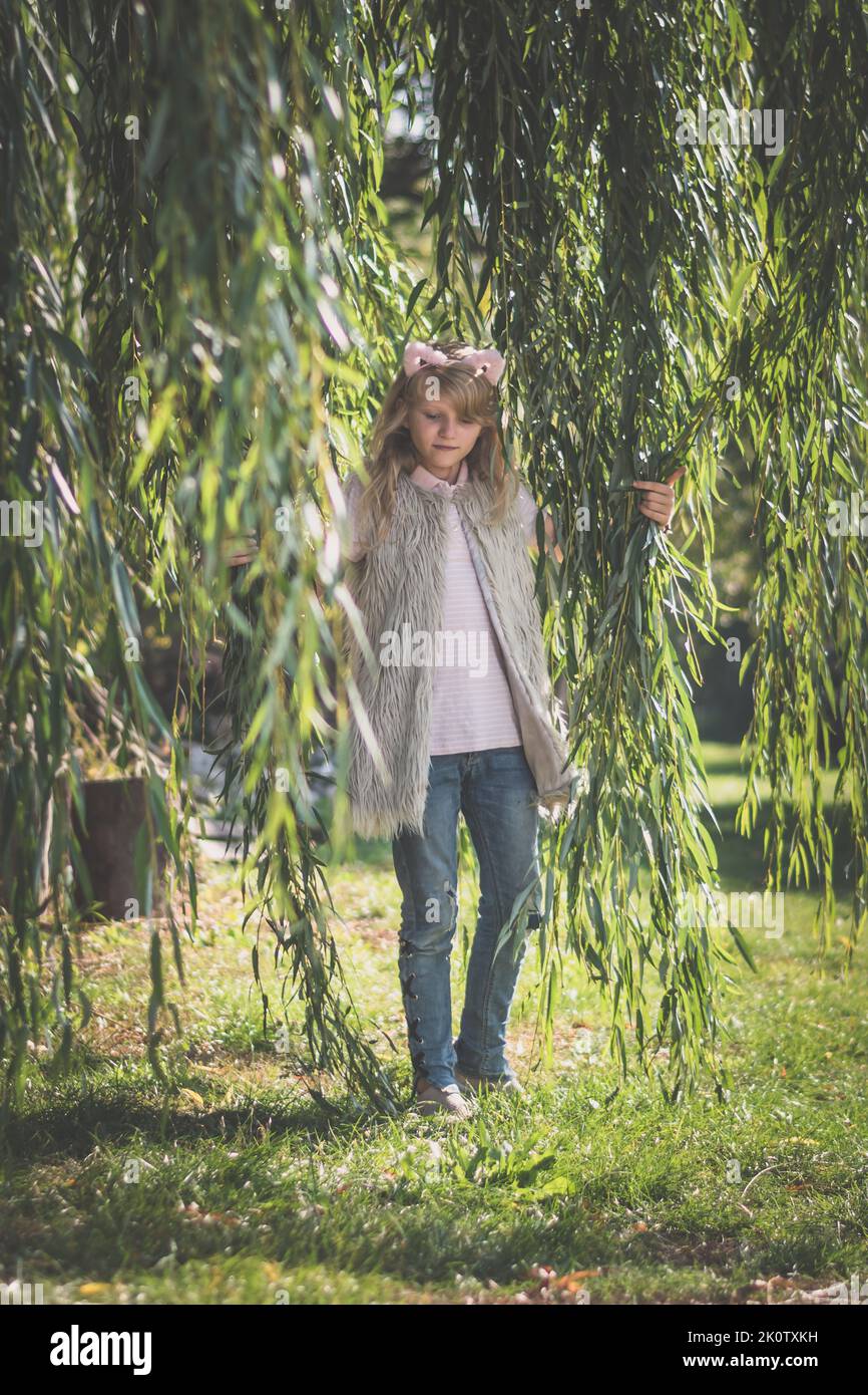 ragazza adolescente carina con lunghi capelli biondi divertirsi con l'albero di salice in primavera all'aperto Foto Stock