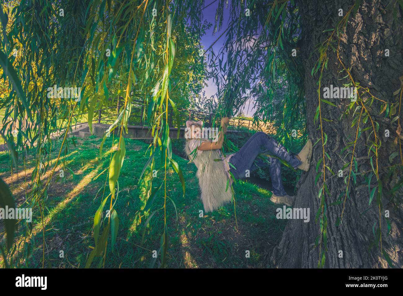 ragazza adolescente carina con lunghi capelli biondi divertirsi con l'albero di salice in primavera all'aperto Foto Stock