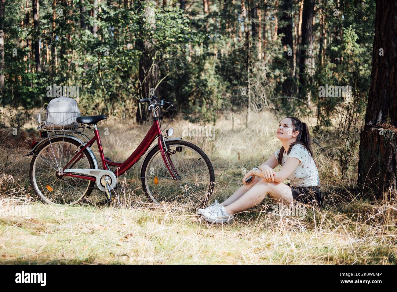 Benefici per la salute mentale del ciclismo, ridurre l'ansia. Ciclismo nella foresta. Piste ciclabili della foresta. Donna singola in bicicletta in pineta nelle giornate di sole. Foto Stock