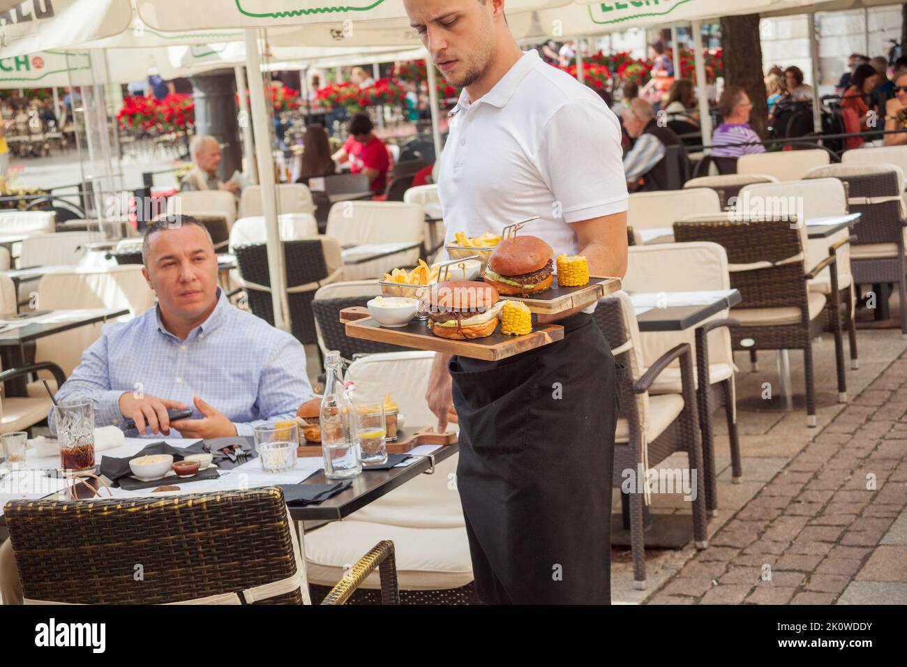 Un cameriere che serve hamburger a un turista seduto a un tavolo all'aperto nella Città Vecchia di Cracovia Polonia Foto Stock