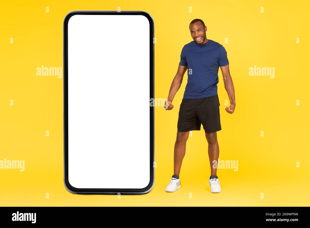 Uomo africano sportivo in posa vicino a enorme schermo telefonico, sfondo giallo Foto Stock