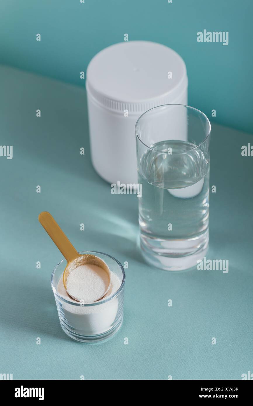 Polvere di collagene in ciotola, bicchiere d'acqua e misurino il cucchiaio su sfondo azzurro Foto Stock