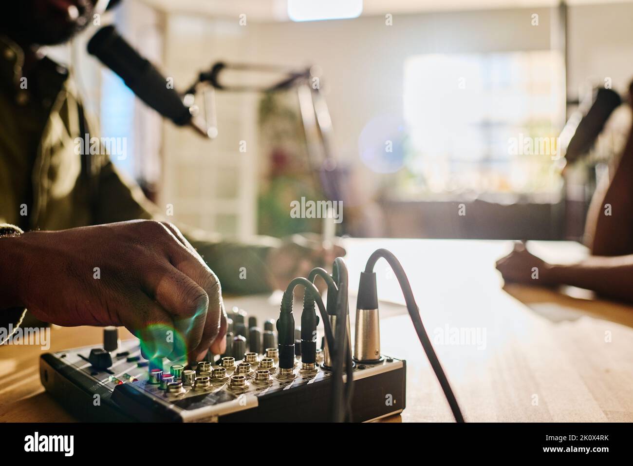 Mano del giovane uomo afroamericano che ruota console sulla soundboard mentre regola il suono prima di registrare un nuovo file audio Foto Stock