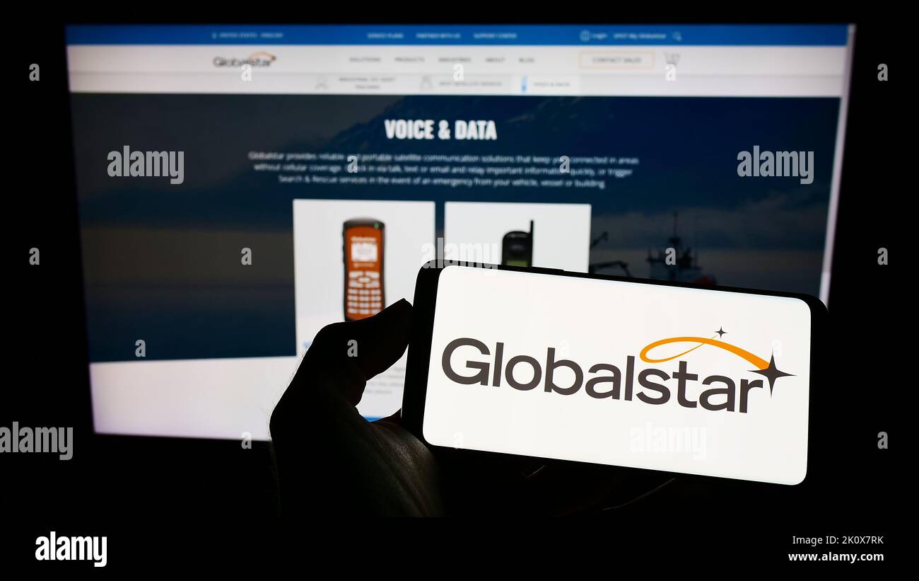 Persona che tiene il cellulare con il logo della società di comunicazioni satellitari Globalstar Inc. Sullo schermo di fronte al sito web. Messa a fuoco sul display del telefono. Foto Stock