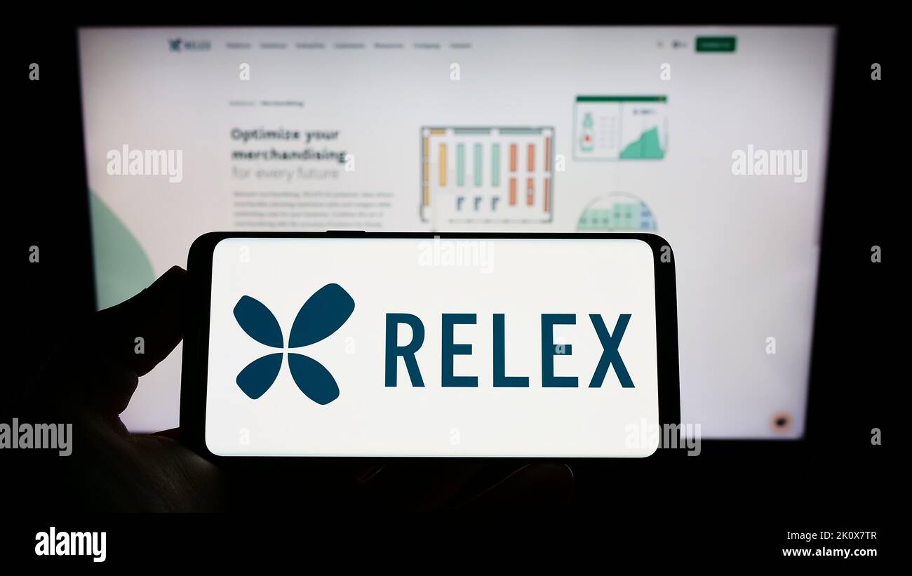 Persona che tiene uno smartphone con il logo della società finlandese di software RELEX Solutions sullo schermo di fronte al sito Web. Messa a fuoco sul display del telefono. Foto Stock