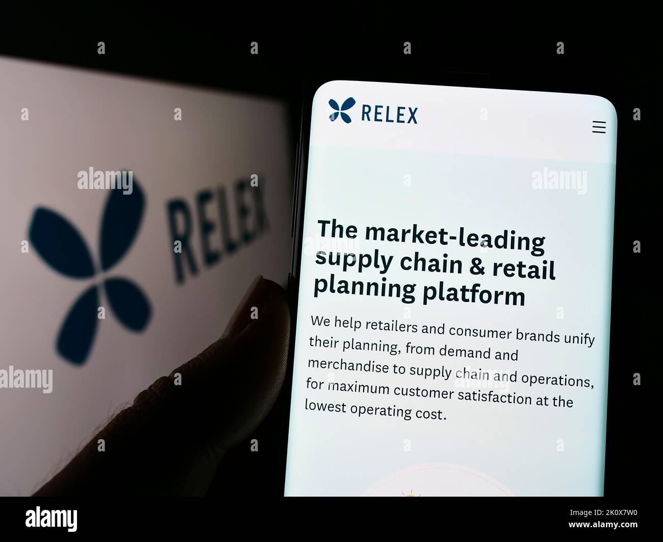Persona che tiene il cellulare con la pagina web della società finlandese di software RELEX Solutions sullo schermo davanti al logo. Messa a fuoco al centro del display del telefono. Foto Stock