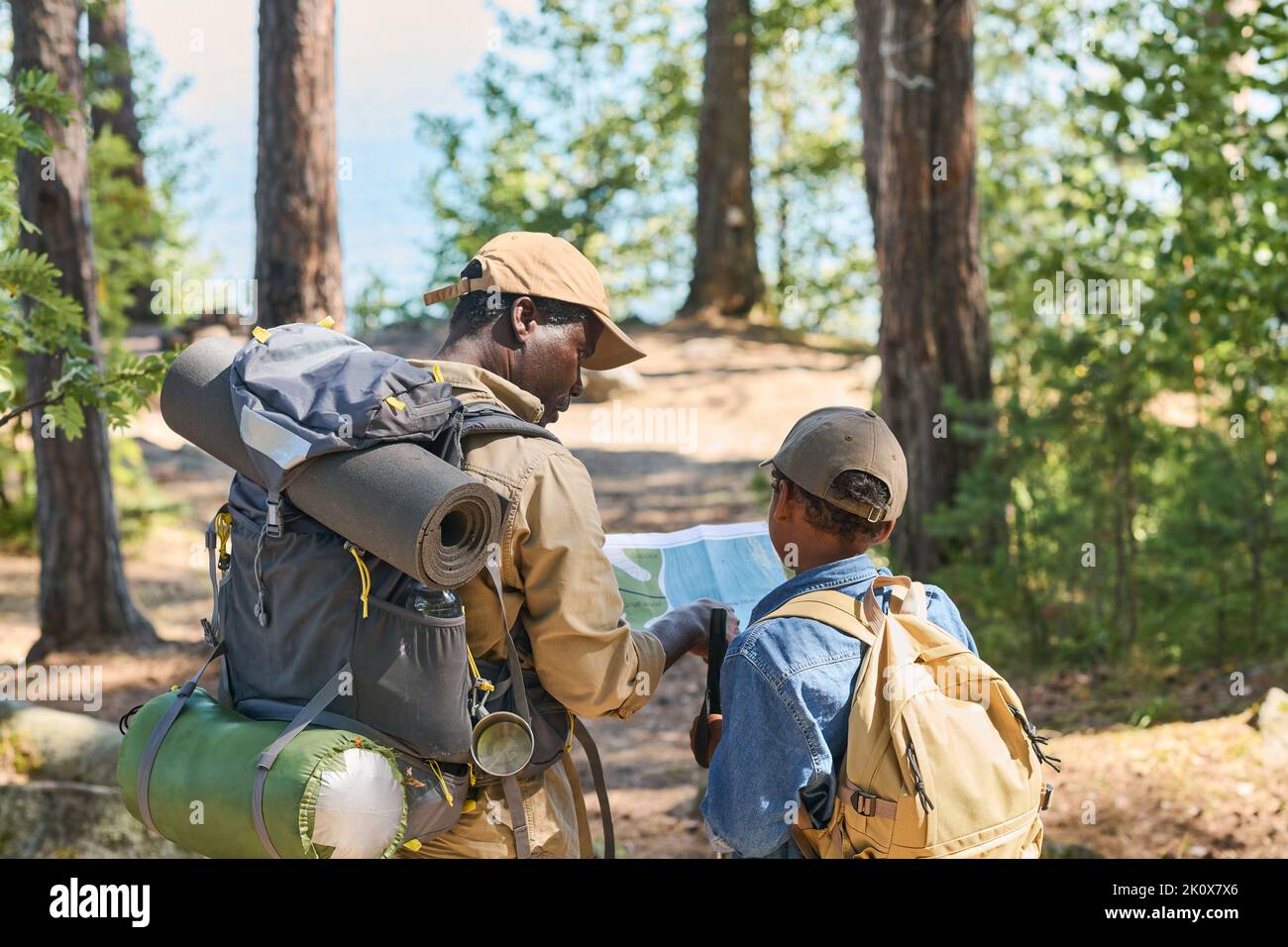 Vista posteriore dell'uomo nero anziano e del suo nipote con zaini che discutono la mappa della zona locale mentre si sposta lungo la foresta Foto Stock