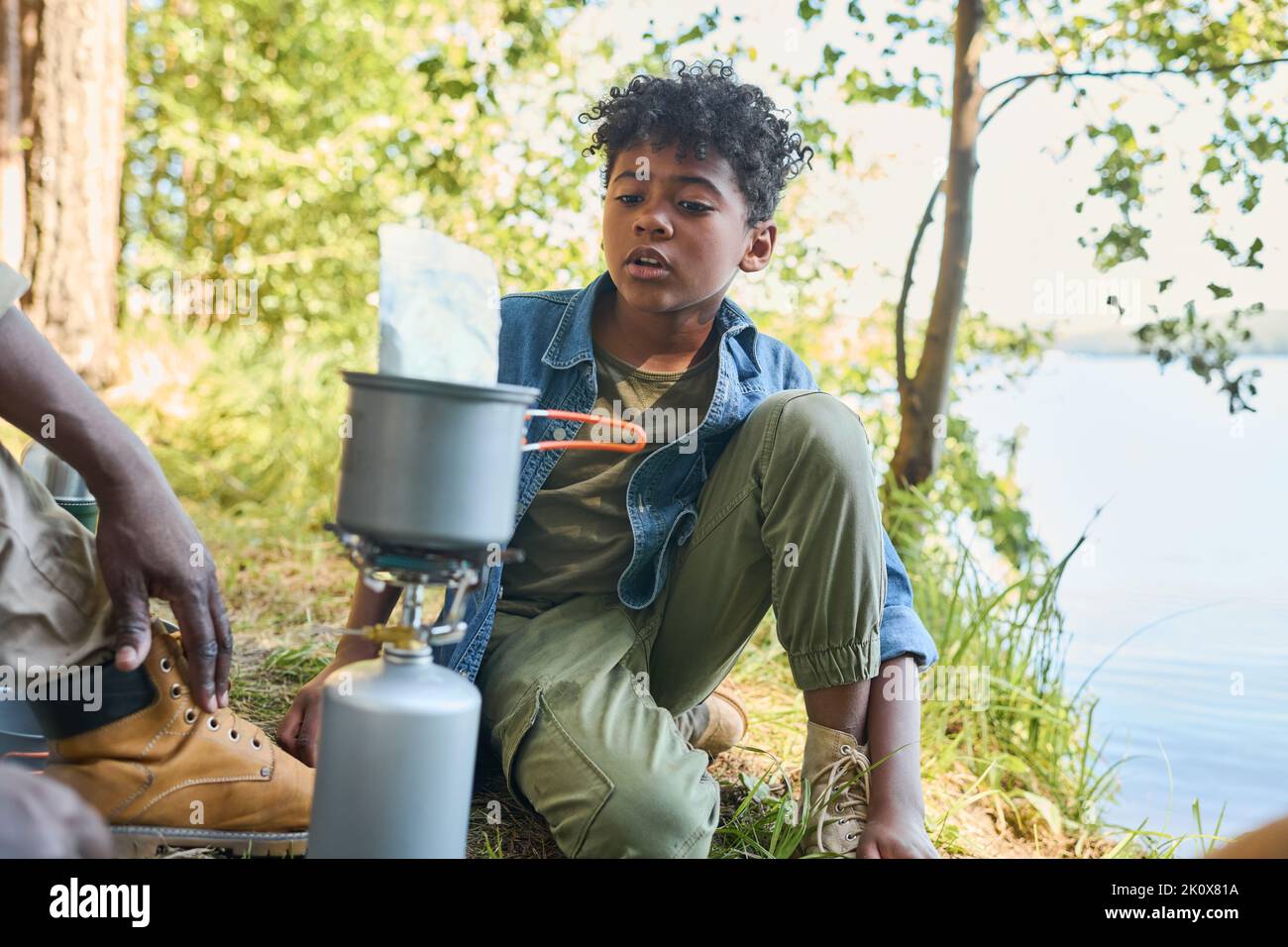 Carino afro-americano pre-teen ragazzo che parla con il nonno mentre si siede di fronte a lui e padella con cibo durante il fine settimana escursione Foto Stock