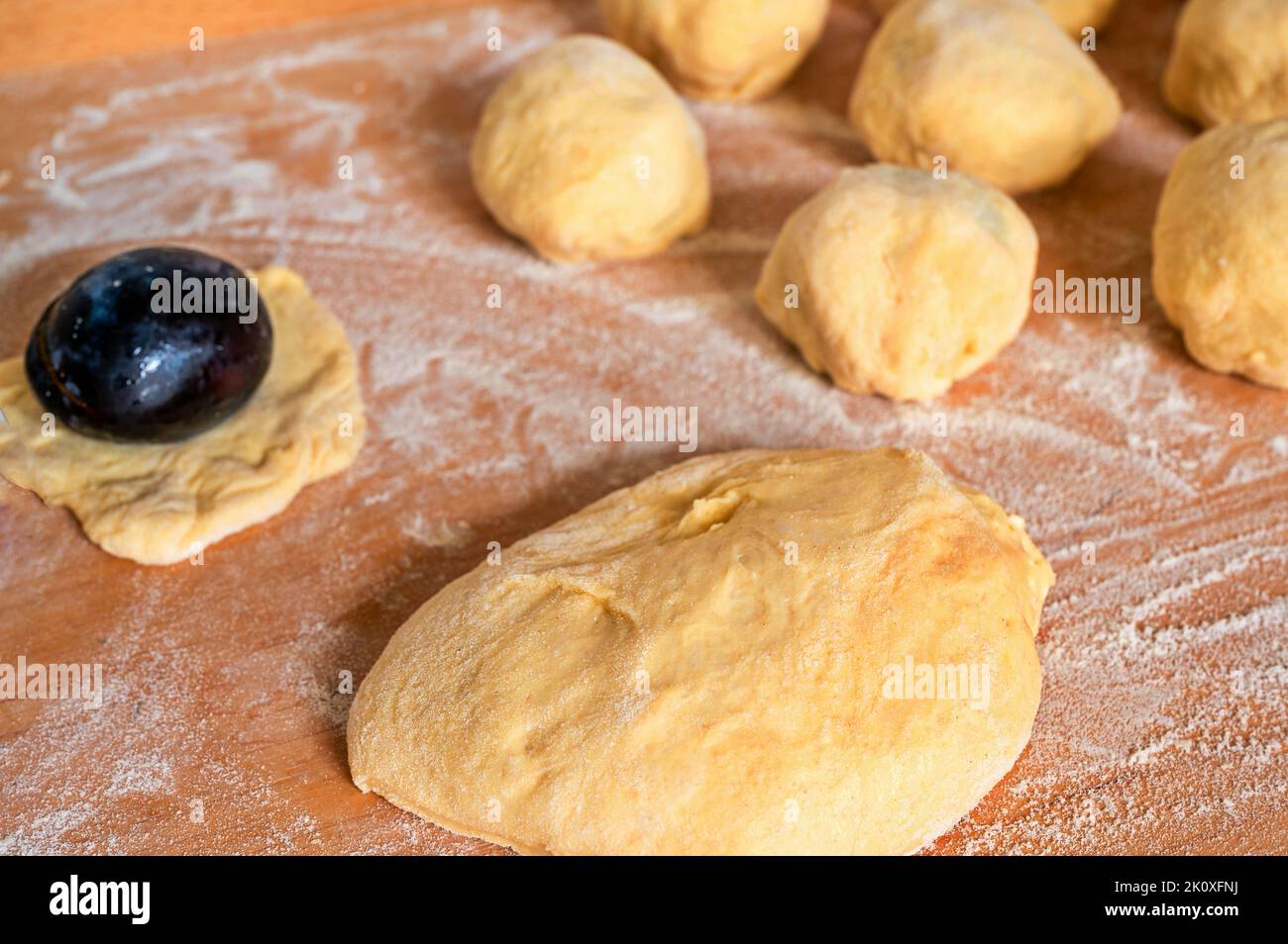 Pezzo di lievito, susina, gnocchi di prugne su tavola di legno da cucina cosparso di farina, primo piano. Preparazione di gnocchi di prugne dolci. Foto Stock