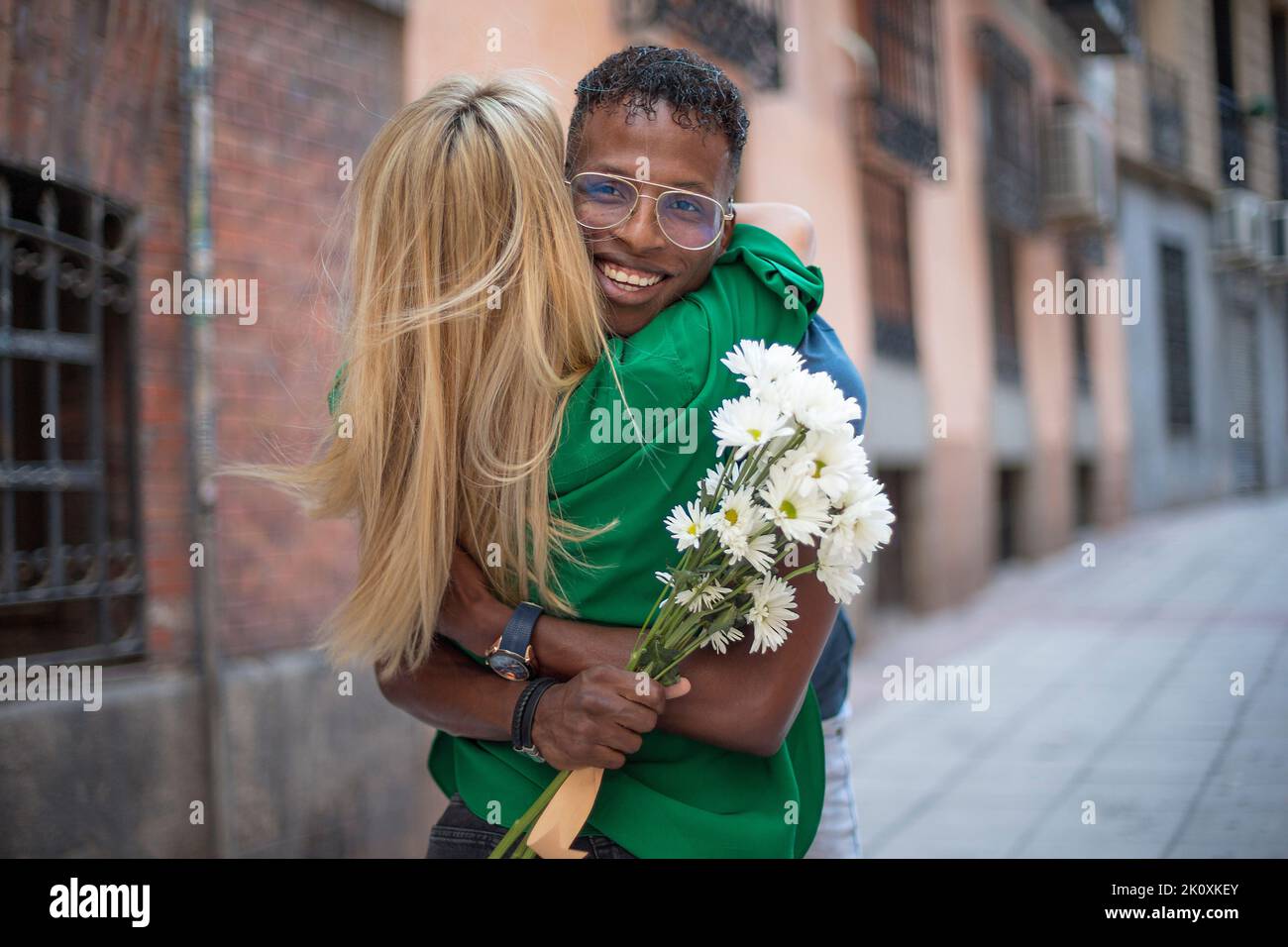 Amici multietnici felici abbracciando mentre tiene un bouquet di fiori in strada Foto Stock