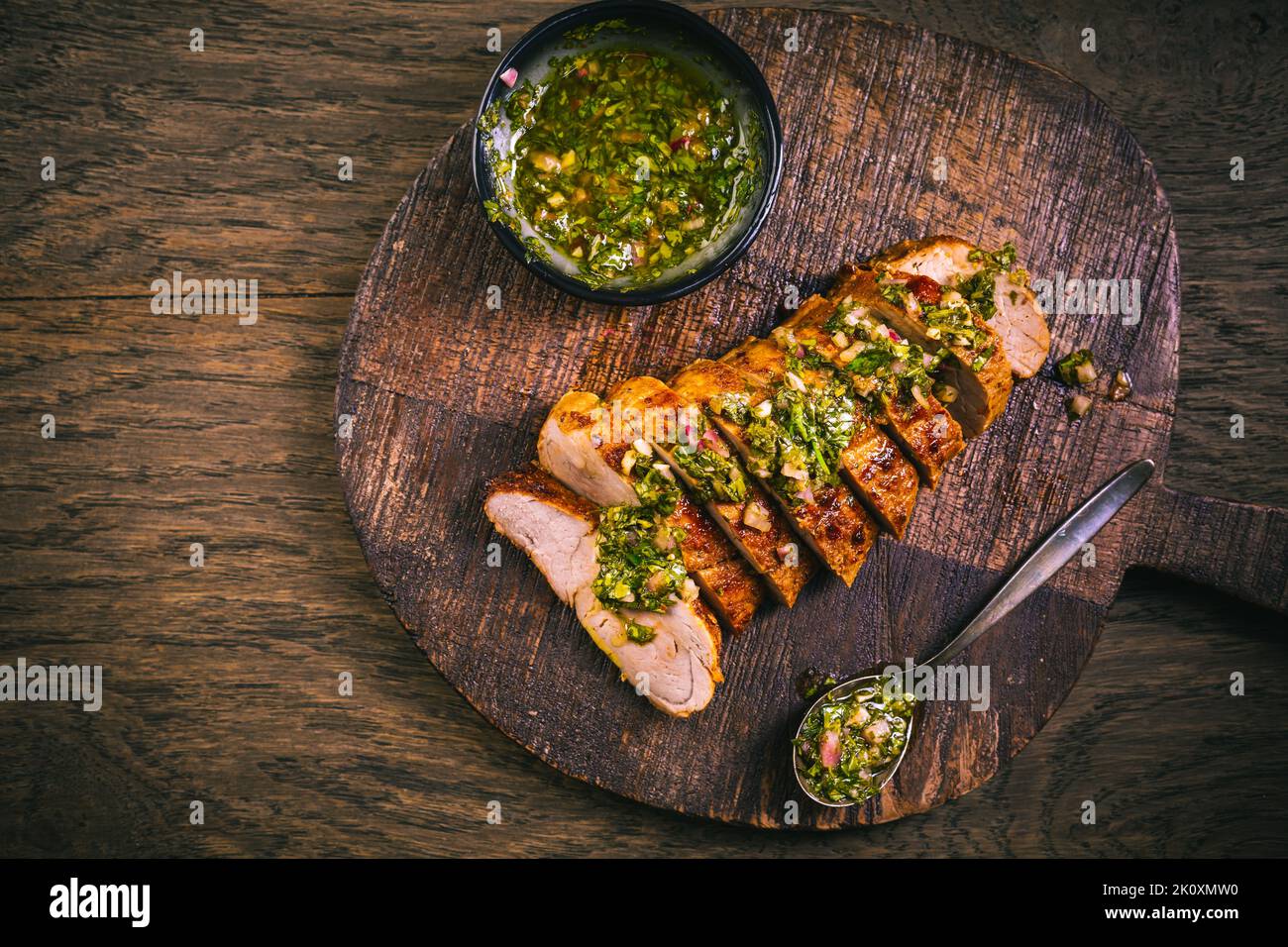 Bistecca di maiale alla griglia fatta in casa con salsa chimichurri verde sul tagliere su sfondo scuro Foto Stock
