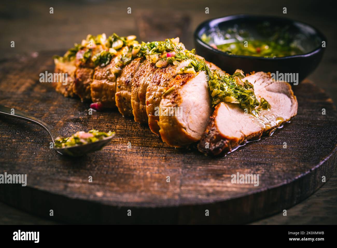 Bistecca di maiale alla griglia fatta in casa con salsa chimichurri verde sul tagliere su sfondo scuro Foto Stock