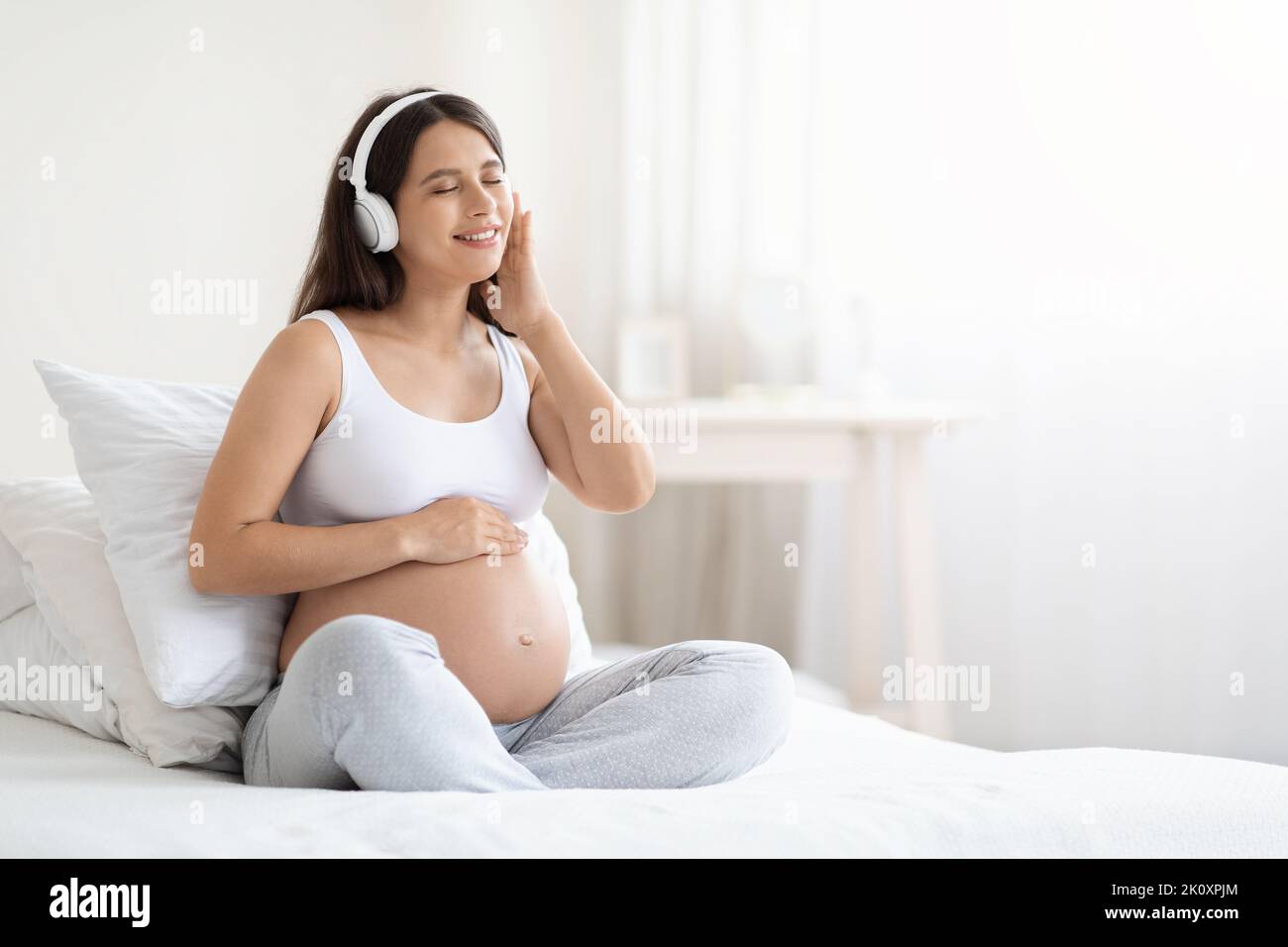 Felice bella giovane donna incinta che ascolta la musica in cuffie Foto Stock