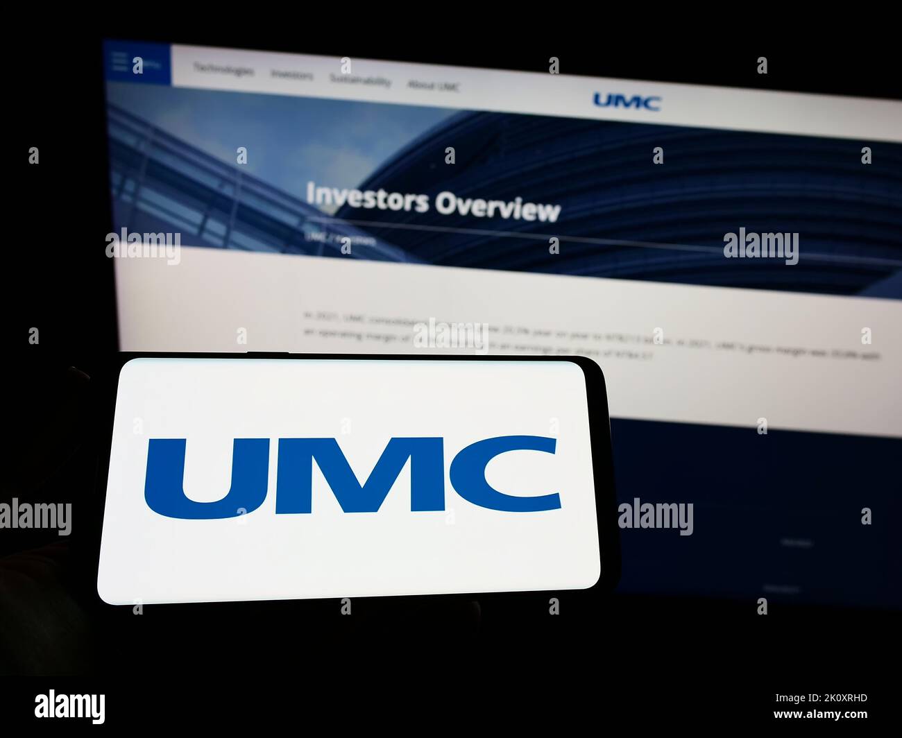 Persona che tiene lo smartphone con il logo della società United Microelectronics Corporation (UMC) sullo schermo di fronte al sito Web. Messa a fuoco sul display del telefono. Foto Stock