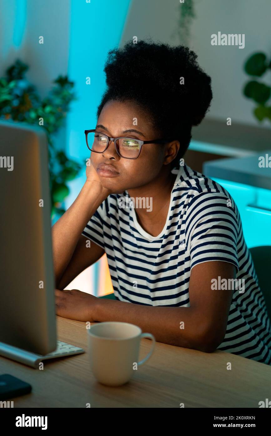 Annoiato African American signora freelancer siede in casa ufficio pensando a progetto guardando al desktop Foto Stock