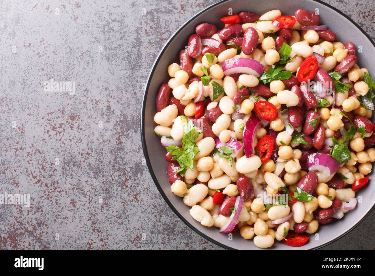 Deliziosa insalata di verdure a tre fagioli con peperoncino e cipolle rosse primo piano in una ciotola sul tavolo. Vista orizzontale dall'alto Foto Stock