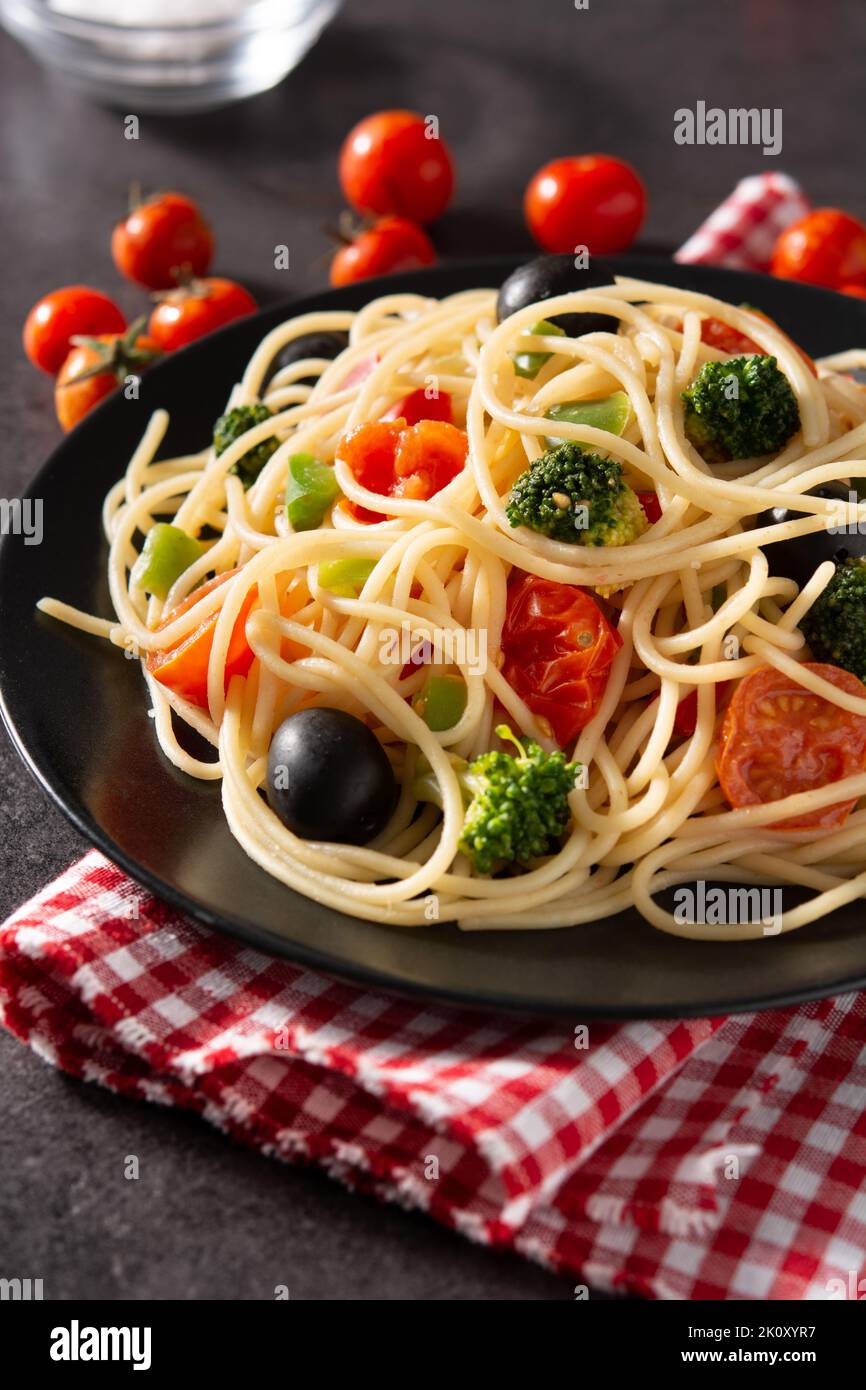 Spaghetti con verdure (broccoli, pomodori, peperoni) su sfondo nero. Primo piano Foto Stock