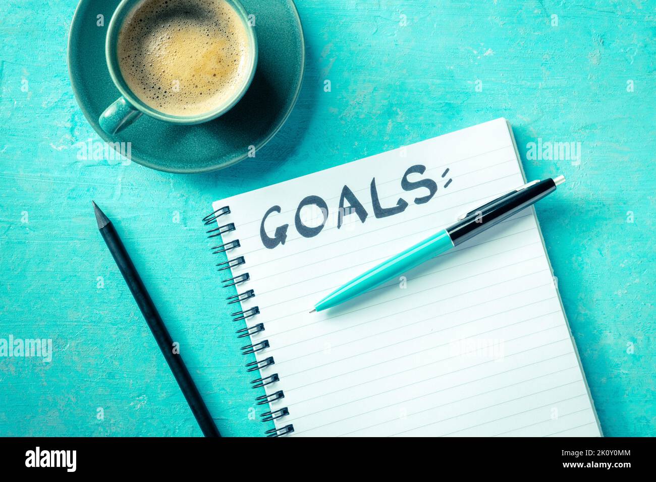 Definizione degli obiettivi. Un notebook con la parola scritta a mano Goals, con una tazza di caffè, una penna e una matita, la testa piatta stesa girato su uno sfondo blu vibrante. Il concetto di scrittura di una lista Foto Stock