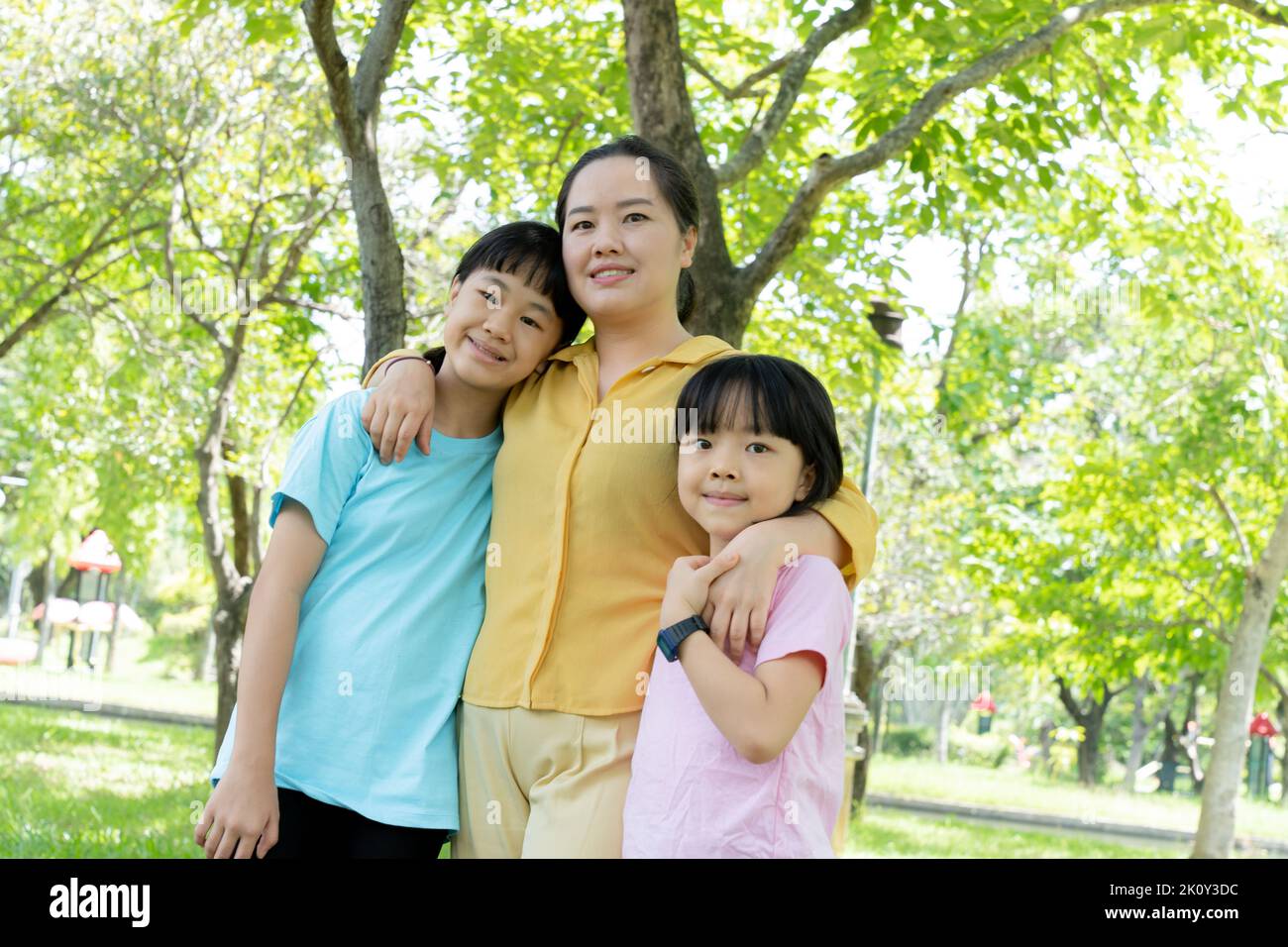 Ritratto di giovane madre e due figlie in fioritura parco verde primavera. Festa di giorno della madre o concetto di giorno della donna Foto Stock