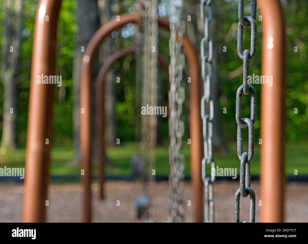 Immagine poco profonda del campo di un parco giochi con altalene e pali di metallo nella luce del mattino presto. Foto Stock