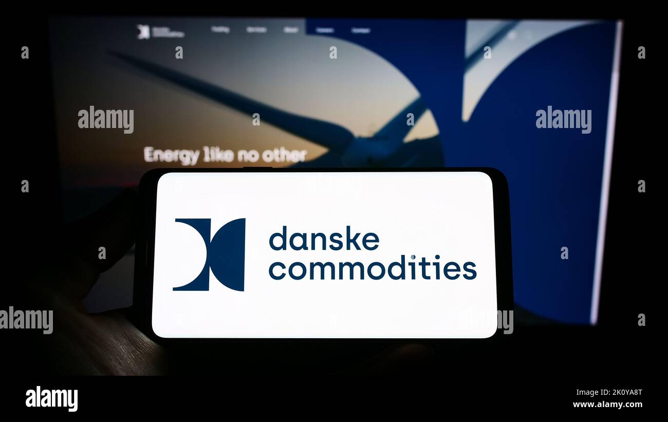 Persona che tiene il cellulare con il logo della società di commercio di energia Danske Commodities COME sullo schermo di fronte al sito web aziendale. Messa a fuoco sul display del telefono. Foto Stock