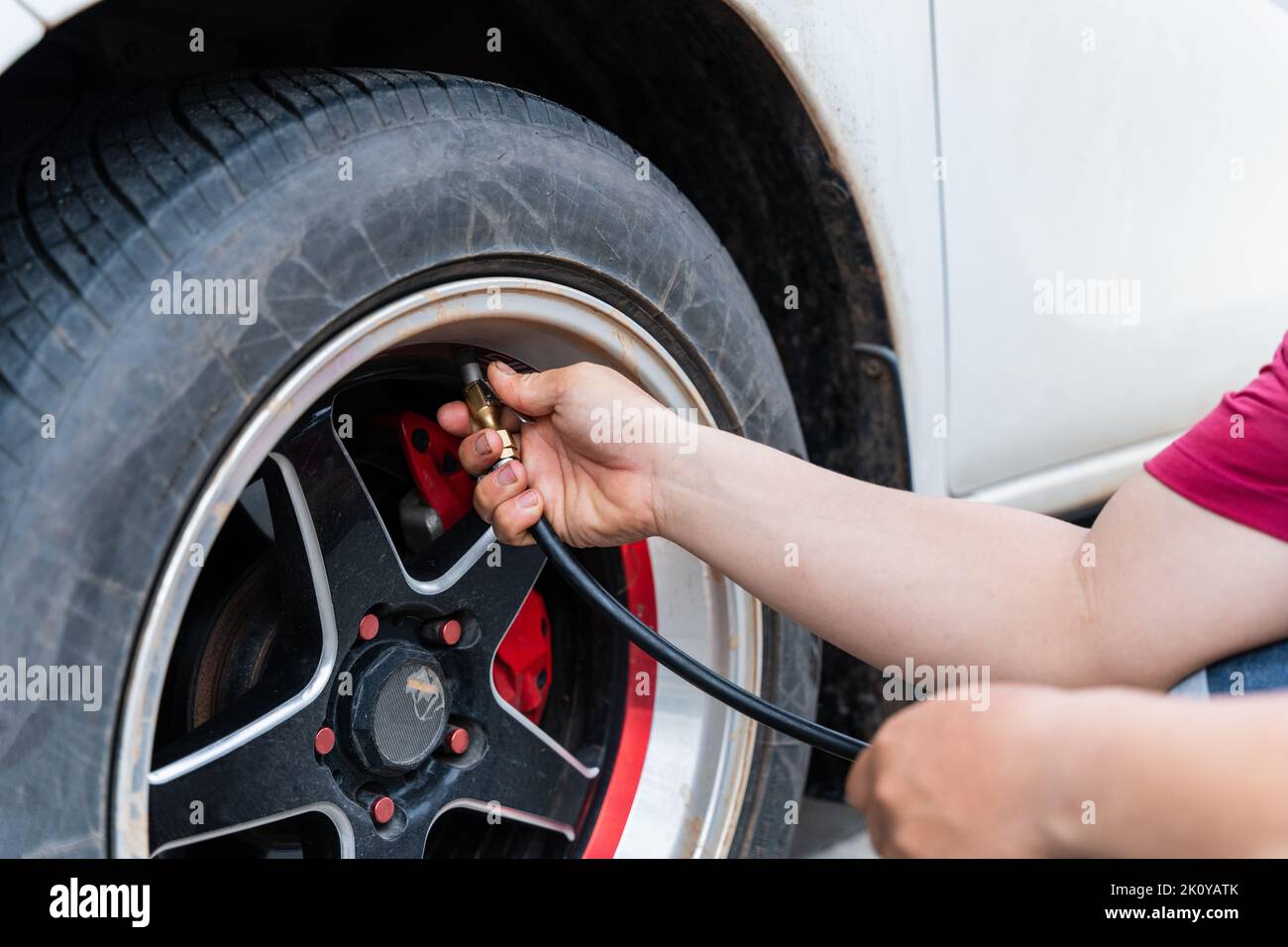 Primo piano di uomo che riempie aria negli pneumatici della sua auto. La mano e la ruota dell'auto aggiungono pressione dell'aria. Foto Stock