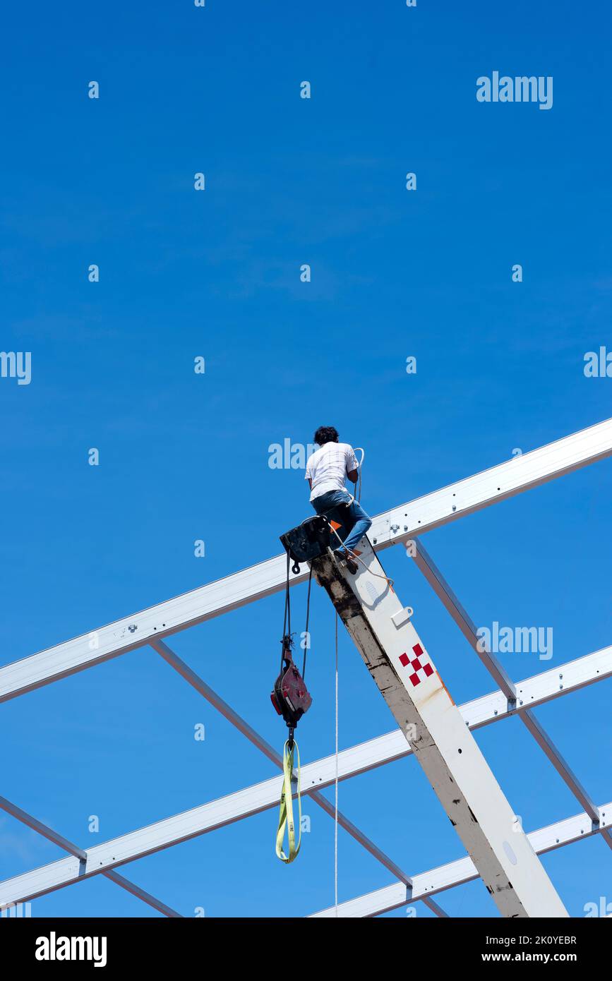Un lavoratore di costruzione, equilibrante sul braccio esteso di una gru contro il cielo blu in Messico Foto Stock