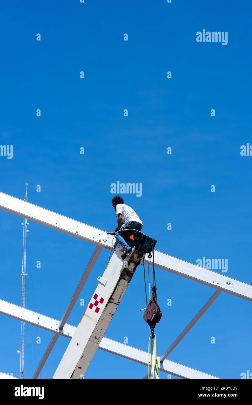 Lavoratore esperto seduto sul braccio esteso di una gru che installa una griglia di copertura in Messico Foto Stock