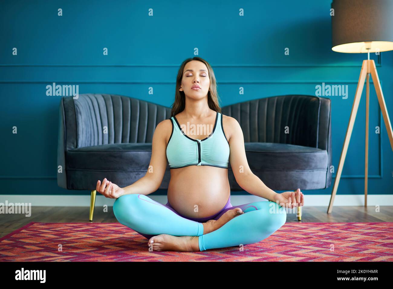 Donna sportiva incinta in abbigliamento sportivo pratica yoga, meditando in Lotus posa Padmasana a casa. Maternità cosciente. Stile di vita sano e cura del bambino Foto Stock