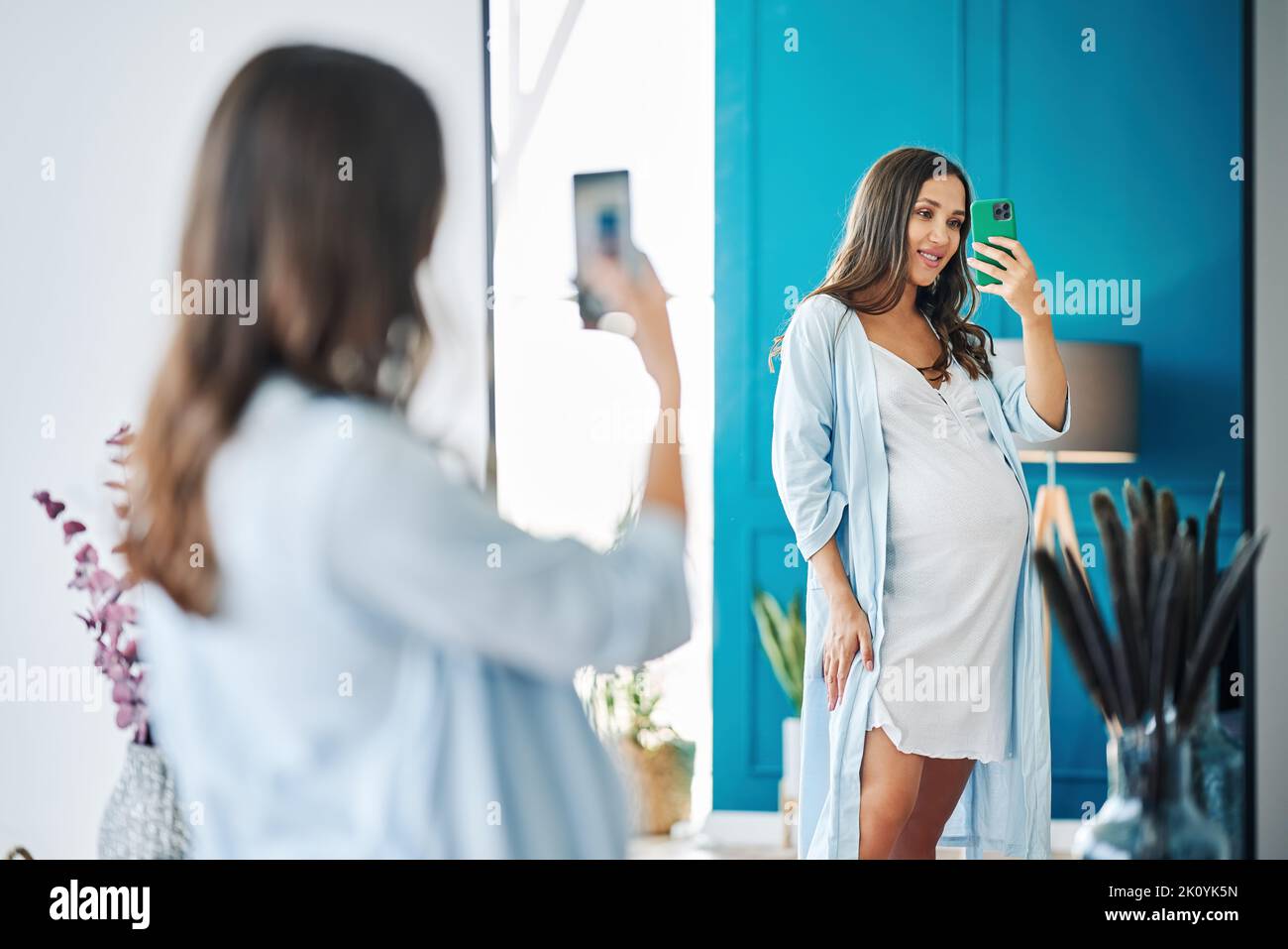 Ritratto di donna incinta sorridente che prende selfie specchio nella casa moderna. Concetto di gravidanza, maternità, aspettativa e tenerezza Foto Stock